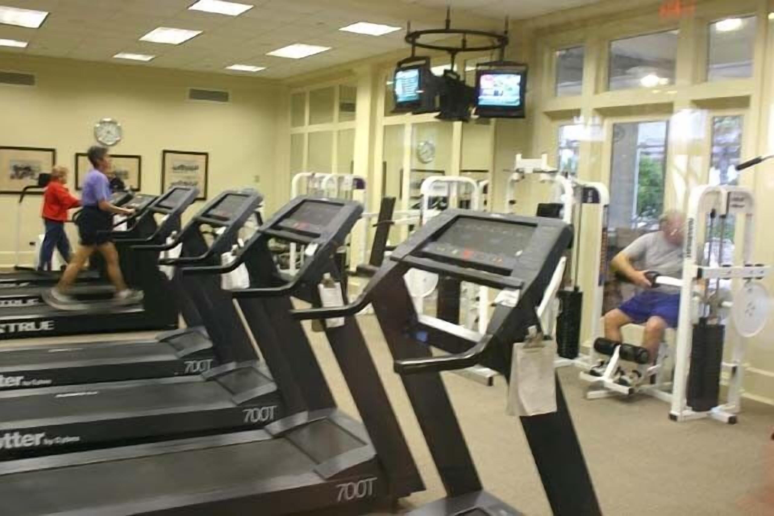 A gym with treadmills, weight machines, and a person using a stationary bike.