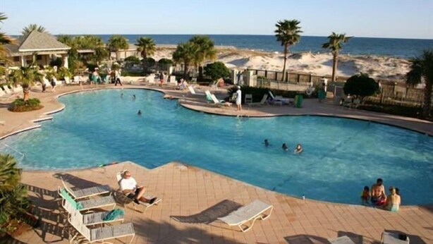 Area piscina con lettini, una piccola vasca e una spiaggia sullo sfondo.