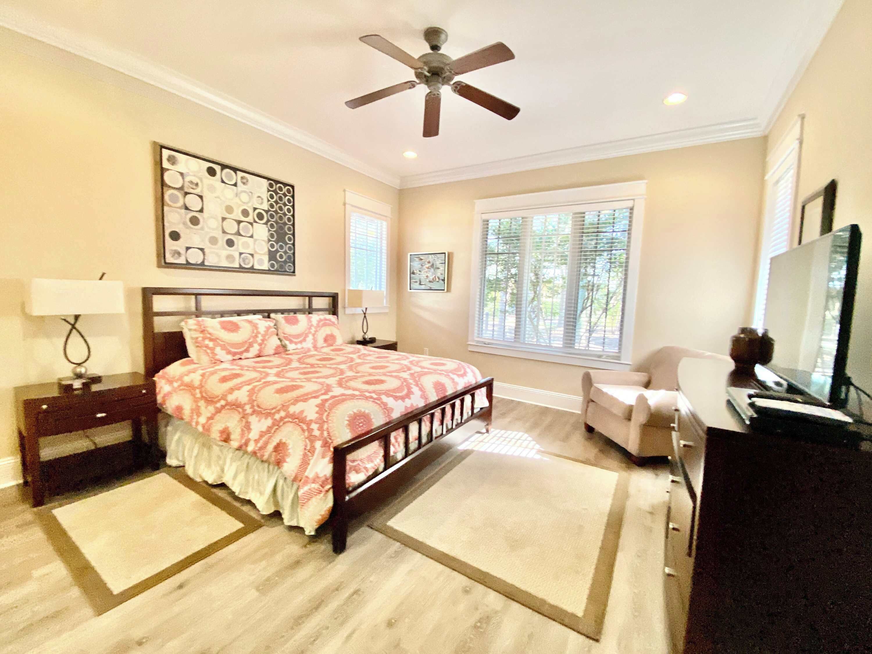 A bedroom with a bed, a desk, a chair, a ceiling fan, and a window.