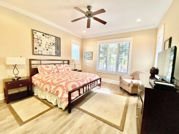 A bedroom with a bed, a desk, a chair, a ceiling fan, and a window.