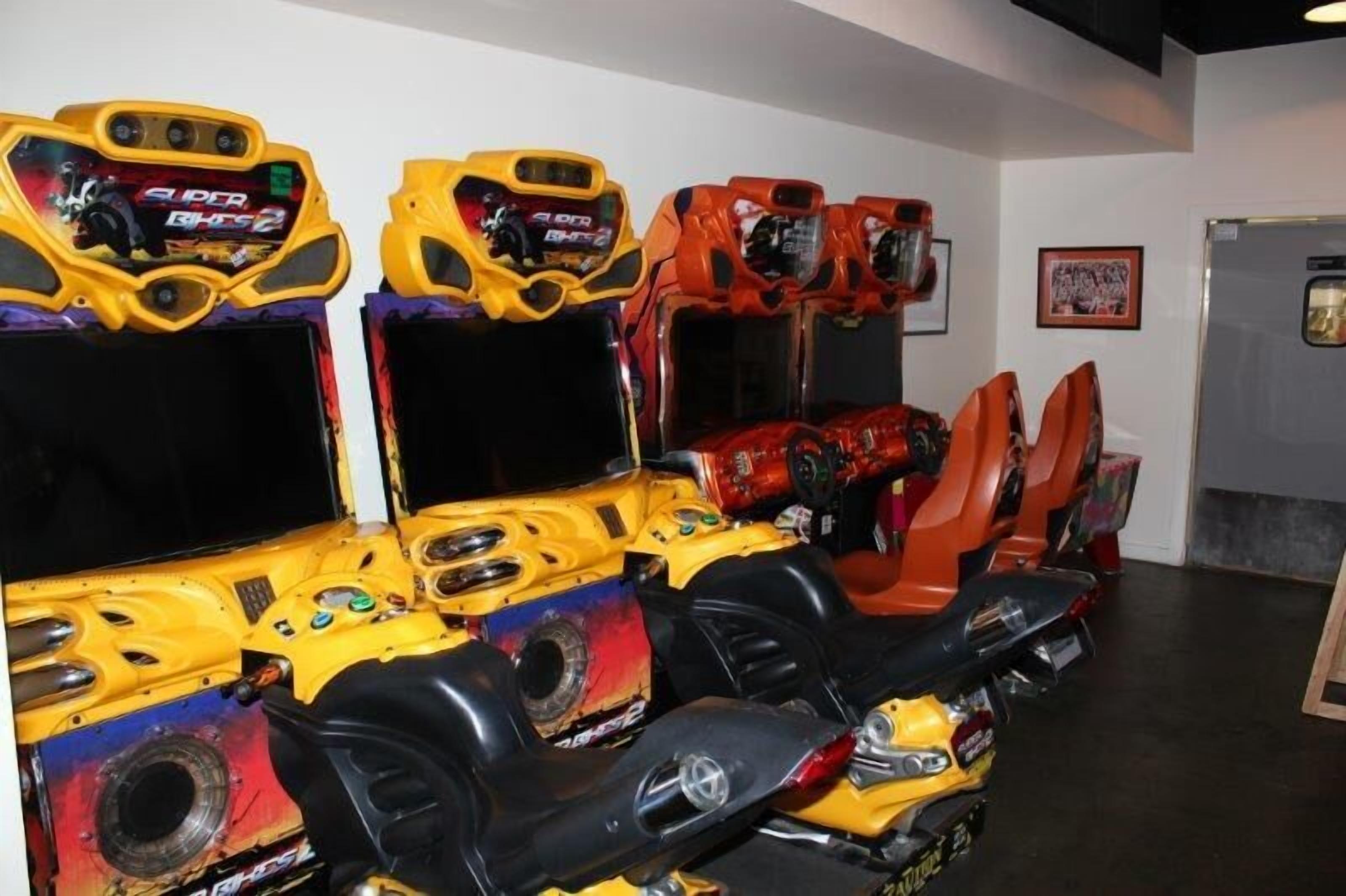 A row of arcade racing game machines with colorful designs and controls.