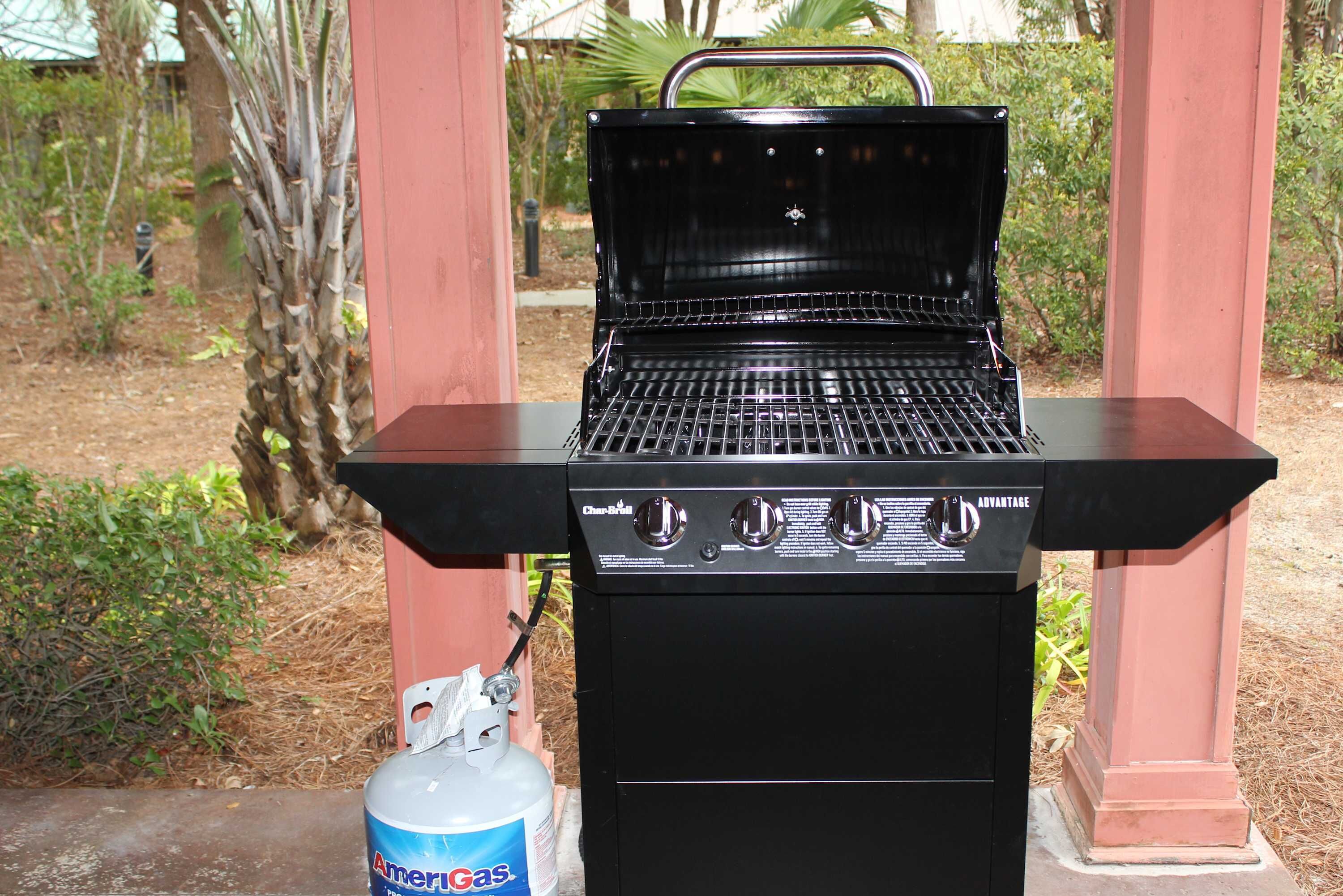 A black charcoal grill with a gas tank attached, placed outdoors.
