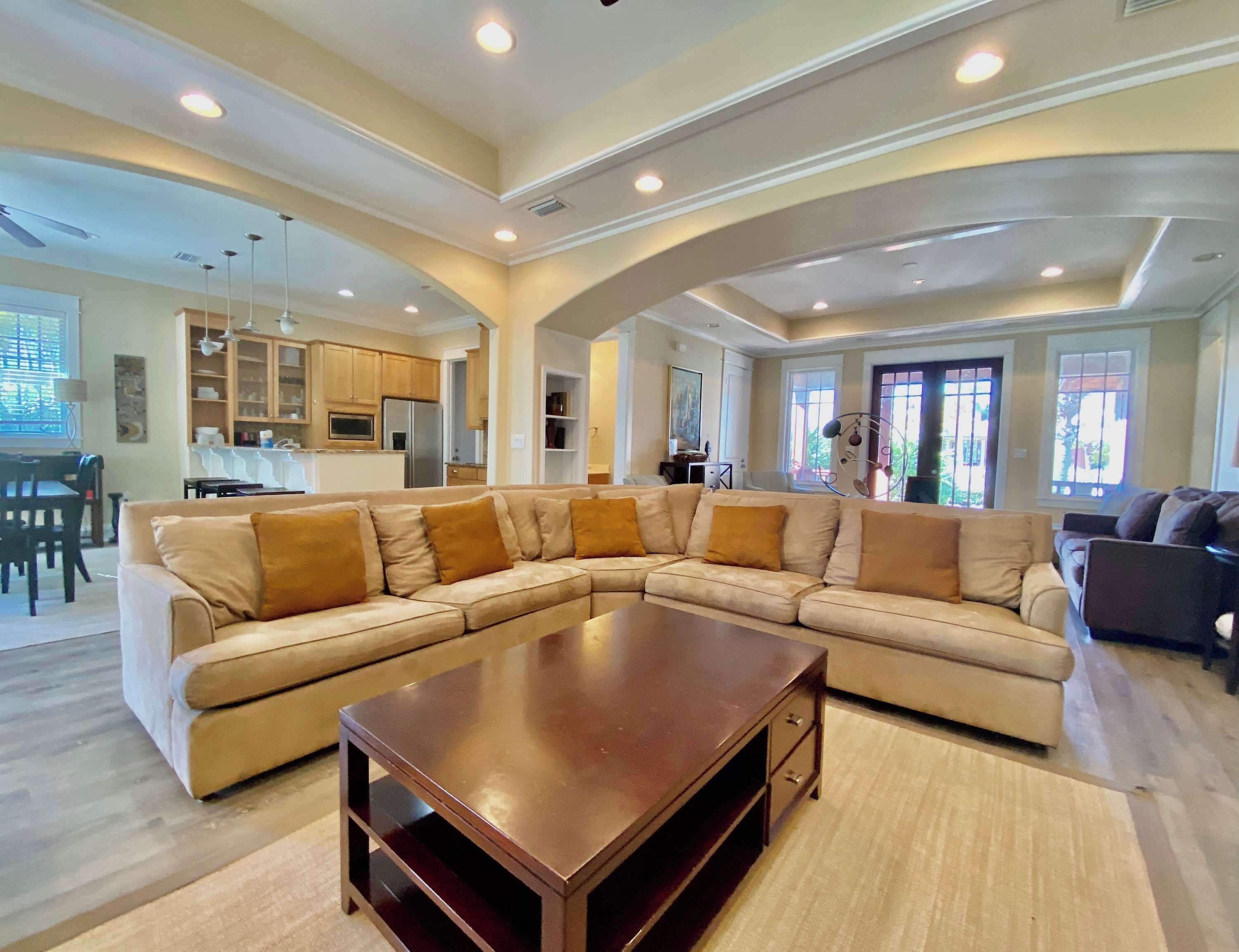 A spacious living room with a large L-shaped sectional sofa, a wooden coffee table, and a kitchen in the background.