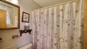 Un bagno con il water, un lavandino, uno specchio e una tenda da doccia con motivo a conchiglia.