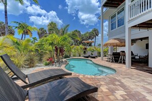 A pool area with lounge chairs, a thatched umbrella, and a white building with large windows.