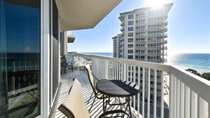 A balcony with a table and chairs, overlooking a beach and a high-rise building. - Open-concept beachfront condo w/ beach service included at Silver Shells! 🌴❤ (Destin)