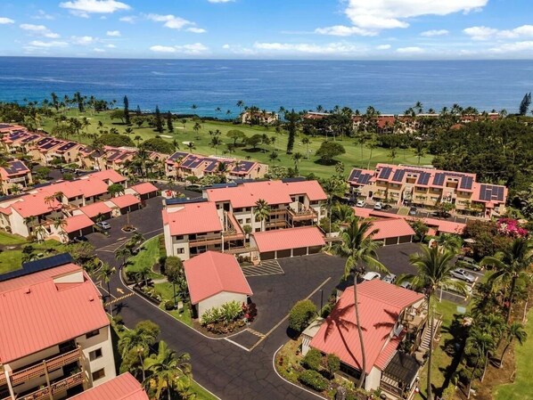 A resort with multiple buildings, a parking area, and a view of the ocean.
