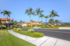 A residential street with palm trees, a stop sign, and houses with red roofs. - Aloha Condos, Kona Coast Resort, Condo 5-102, Fairway Front, AC (Kailua Kona)