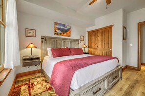 A bedroom with a bed, bedside lamps, a wooden wardrobe, a painting on the wall, and a patterned rug. - Free SkyCard Activities - Gas Fireplace, Parking, Equipped Kitchen, Fitness Ctr (Breckenridge)