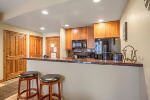 A kitchen with wooden cabinets, a stainless steel refrigerator, a microwave, and a granite countertop.