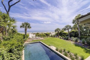 Una piscina con vista al océano, rodeada de exuberante vegetación y un césped bien cuidado.