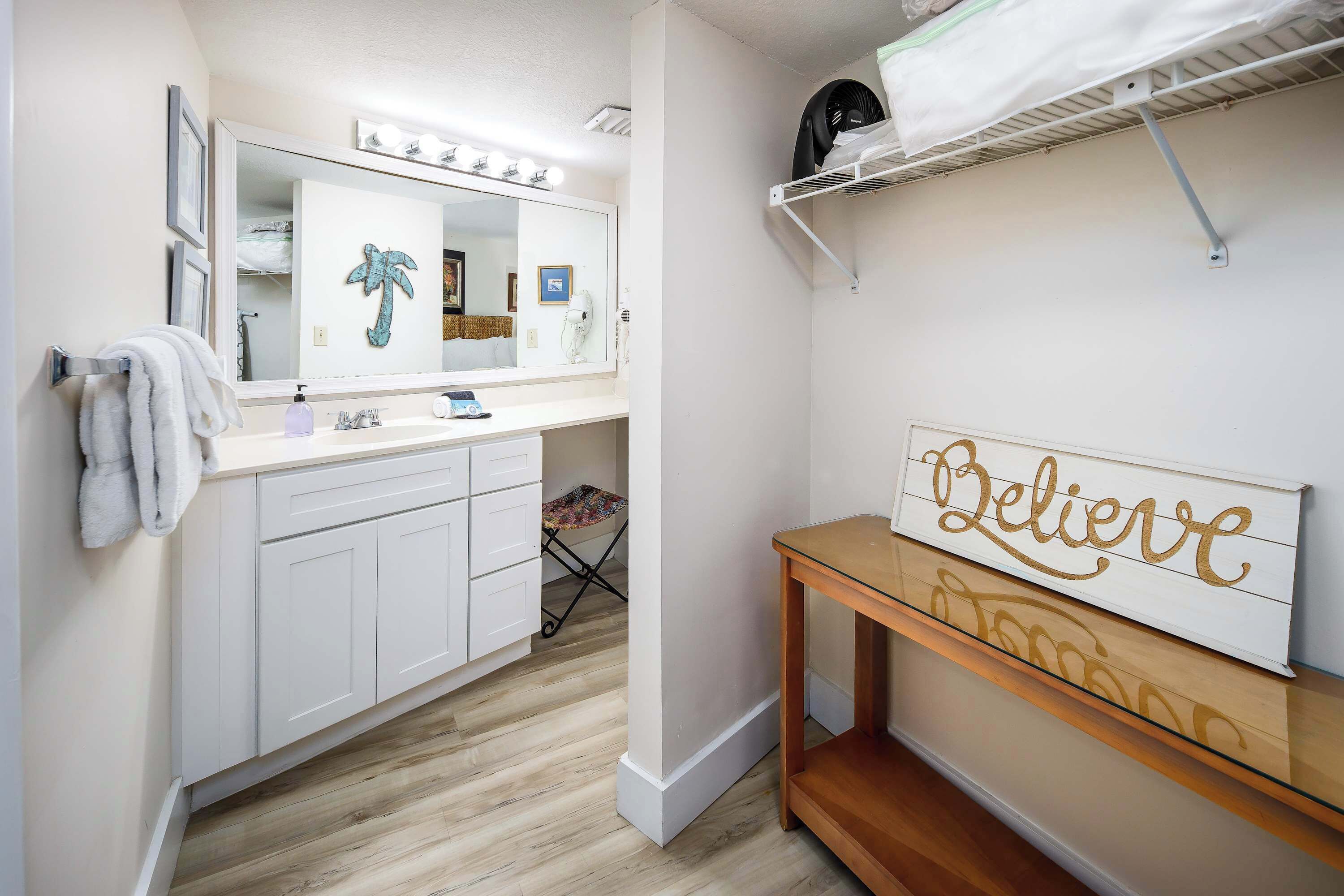 A bathroom with a vanity, mirror, towel rack, and a motivational sign.
