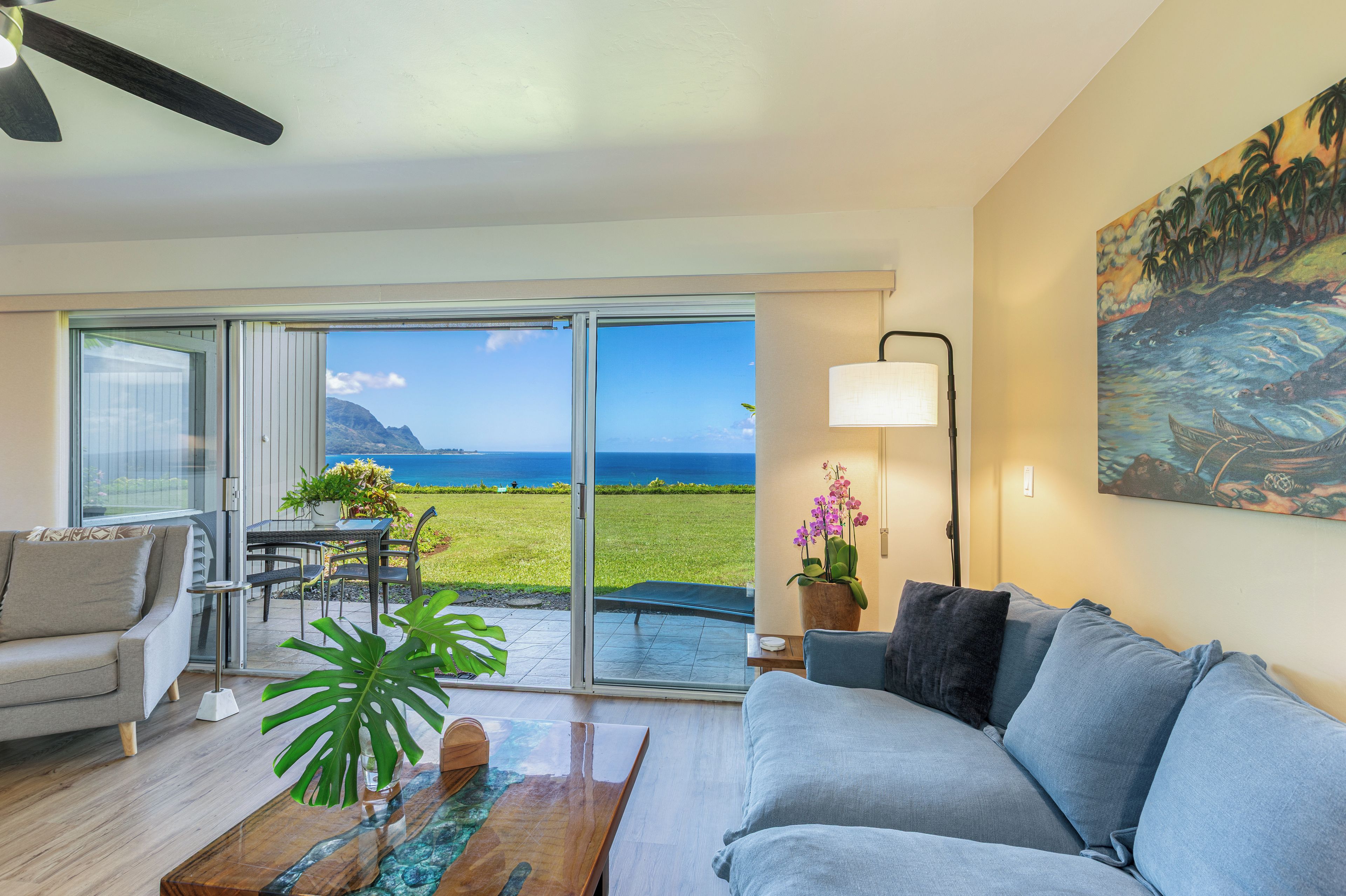 A living room with a sofa, a coffee table, and a view of the ocean through a sliding door.