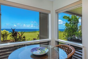 A room with a glass table and a bowl, overlooking a grassy area and the ocean.