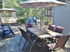 An outdoor patio with a table and chairs, a covered umbrella, and a barbecue grill. - 3 Killdeer - Remodeled! Close to Village, SHARC Passes, Hot Tub, Bikes, Luxury Linens (Sunriver)