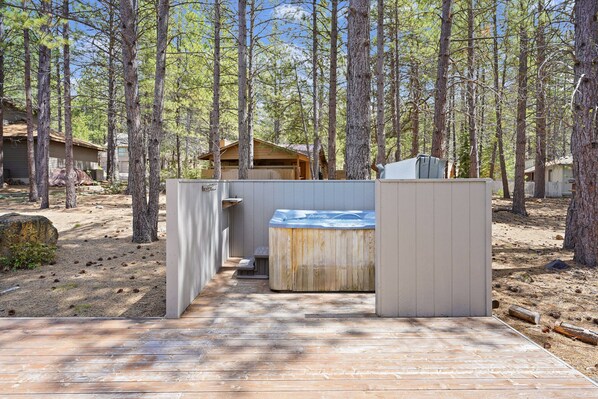 A wooden deck leading to a hot tub area surrounded by tall pine trees.