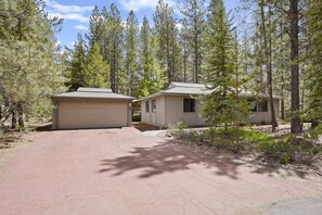 A two-story mobile home with a garage, surrounded by a forested area. - 3 Killdeer - Remodeled! Close to Village, SHARC Passes, Hot Tub, Bikes, Luxury Linens (Sunriver)