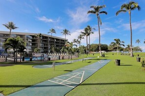 A courtyard with a shuffleboard court, palm trees, and a modern building with balconies.