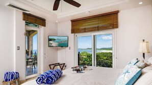 Une chambre dotée d’un grand lit, d’une télévision, d’un balcon avec vue sur la plage et d’un ventilateur de plafond.