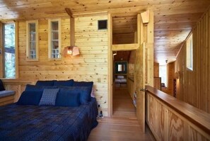 Ein Holzhütten-Innenraum mit einem Bett, Fenstern und einer Treppe.