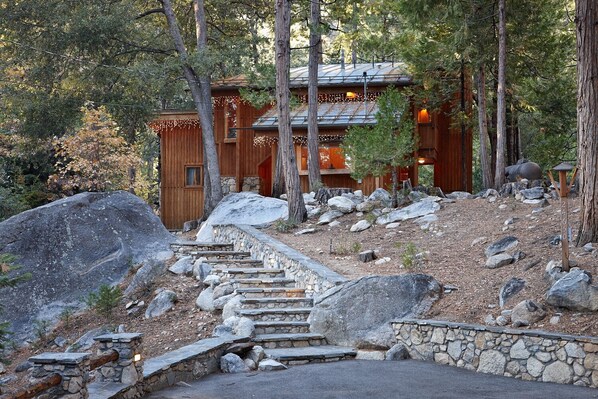 A wooden cabin with a stone staircase leading to the entrance, surrounded by trees and rocks.