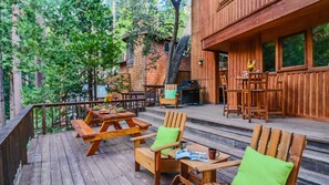 Eine Holzterrasse mit Picknicktischen und -stühlen, einem Grill und einem Holzzaun.