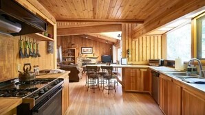 Ein Holzblockhaus-Interieur mit einer Küche, die einen Herd, Barhocker und einen Esstisch beinhaltet.
