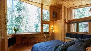 Ein gemütliches Blockhausszimmer mit einem Bett, einem kleinen Schreibtisch und einem Fenster mit Blick auf einen Wald.