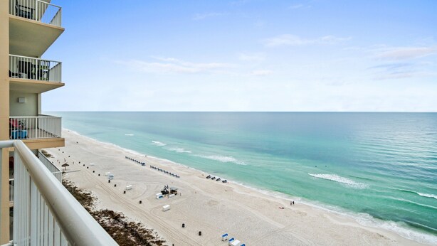 Une vue sur la plage depuis un balcon, avec un ciel dégagé, une plage de sable et l’océan.