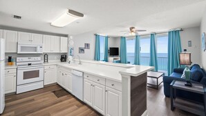 Une cuisine moderne avec des meubles blancs, un îlot central et un coin repas comprenant un canapé bleu et une table.