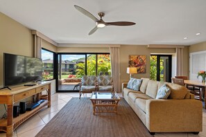 A modern living room with a flat-screen TV, wicker coffee table, and a sofa. - Wailea Elua 2003 - Ground Level Gem -Oceanfront Property W/ Tropical Grounds (Wailea, Maui)