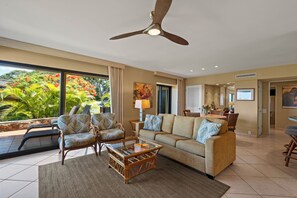 Un salón amplio con un ventanal grande, un ventilador de techo, un sofá, dos sillones y una mesa de centro.