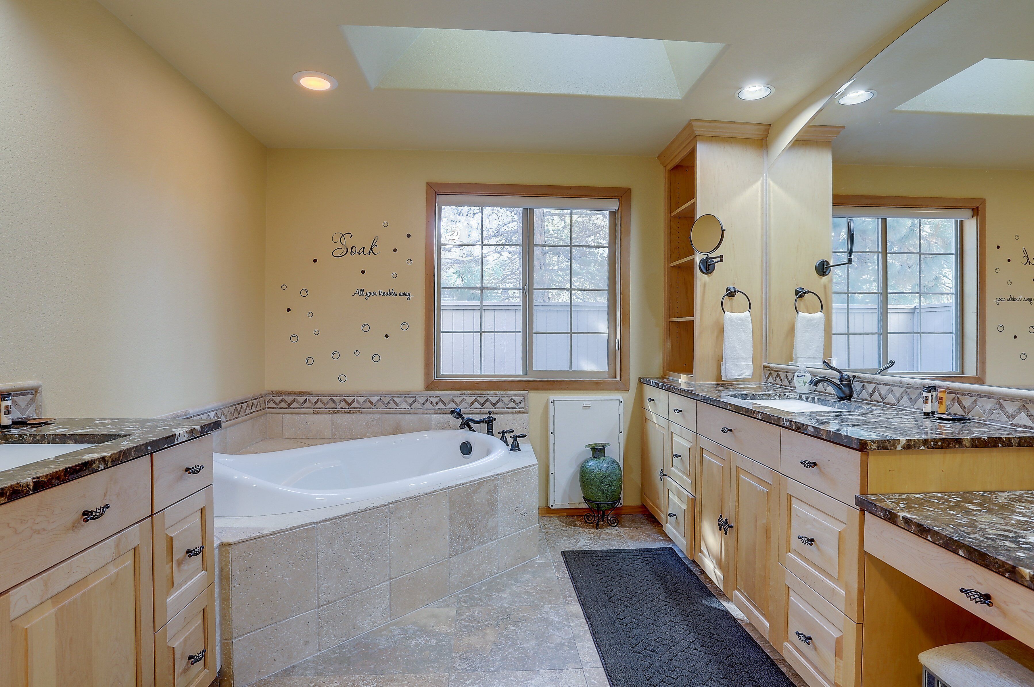 Un baño amplio con una bañera grande, tocador doble con espejos y ventana que proporciona luz natural.