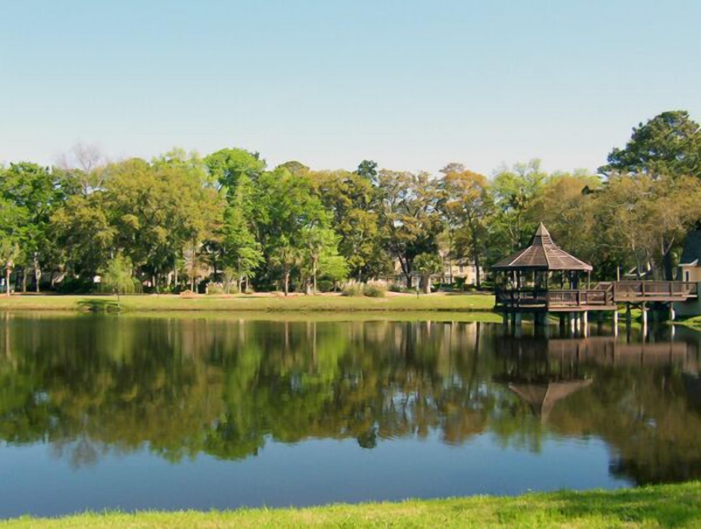 Un parque tranquilo con un estanque, un pabellón y una pasarela de madera sobre el agua.