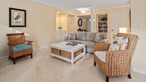 Una sala de estar con muebles de mimbre, una mesa de centro blanca y una estantería.