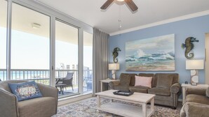 Ein Wohnzimmer mit großem Fenster, Deckenventilator, Sofa, Couchtisch und einem Gemälde vom Meer.