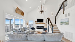 A spacious living room with a large gray sofa, a chandelier, and a staircase leading to an upper level. - Gulf Front | Pet Friendly | Shared Pool (Gulf Shores)