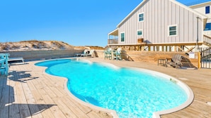 A wooden deck with a swimming pool, lounge chairs, and a large building with a balcony. - Gulf Front | Pet Friendly | Shared Pool (Gulf Shores)