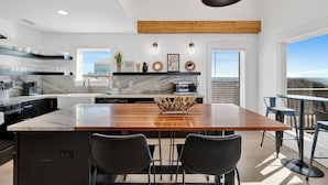 A modern kitchen with a wooden island, black chairs, and a view of the ocean. - Gulf Front | Pet Friendly | Shared Pool (Gulf Shores)
