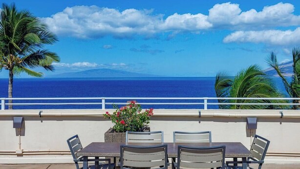 Un balcón con mesa y sillas, con vistas a la costa, palmeras y el océano.