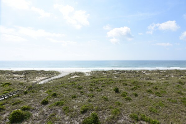 A coastal landscape with a sandy beach, grassy dunes, and a wooden walkway leading to the beach.