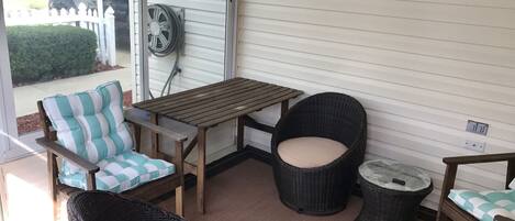 A covered patio area with wicker furniture, a wooden table, and a view of a vehicle outside.