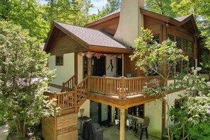 A wooden cabin with a balcony, a covered deck, and a patio area with outdoor seating.