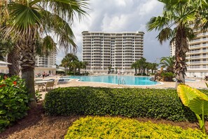 A hotel with a large pool, palm trees, and a multi-story building in the background. - Live the High Life: Luxe 11th Floor Gulf Front Condo Awaits Your Arrival! (Destin)