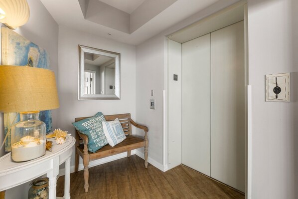 A room with a wooden bench, a lamp, a mirror, and a white door. - Live the High Life: Luxe 11th Floor Gulf Front Condo Awaits Your Arrival! (Destin)
