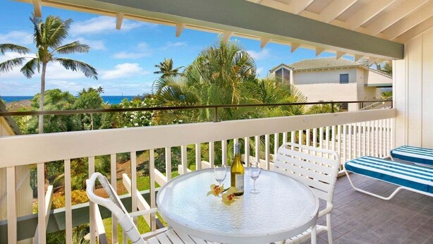 A round table with two chairs and a bottle of wine, overlooking a tropical landscape with palm trees and a view of the ocean. - Manualoha 305 Poipu Beach By Suite Paradise (Koloa)