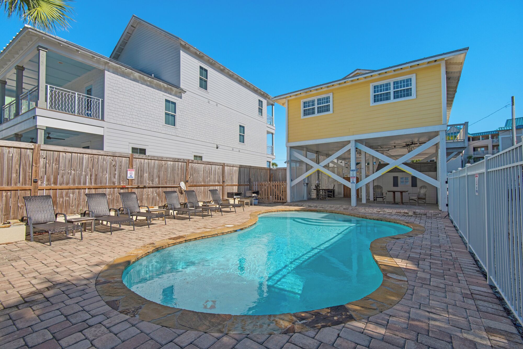 A swimming pool with a wooden deck, a fenced area, and two buildings with balconies.