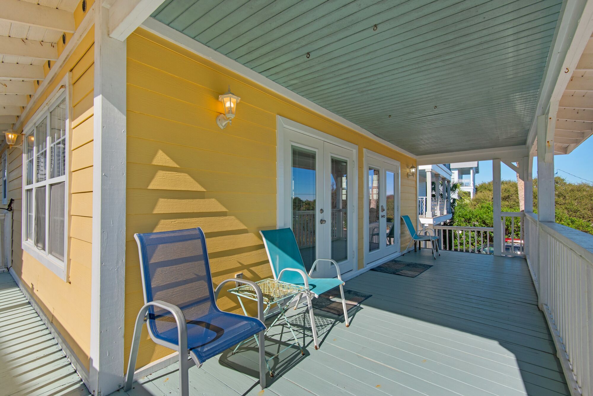 A covered porch with two chairs and a table, a door with a glass panel, and a railing.