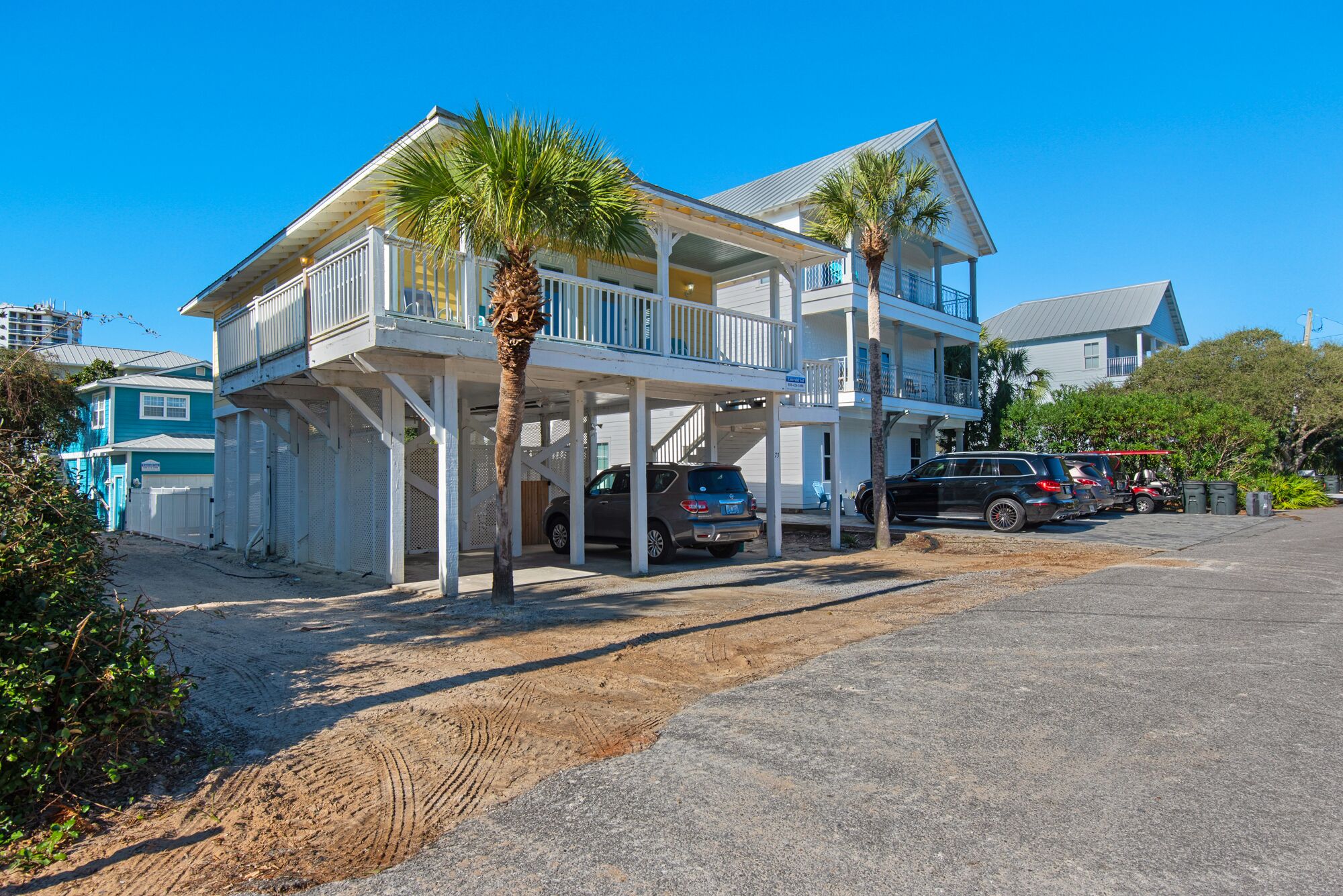 Ein zweistöckiges Strandhaus mit überdachter Veranda, einer Garage und einem Parkplatz mit mehreren Autos.