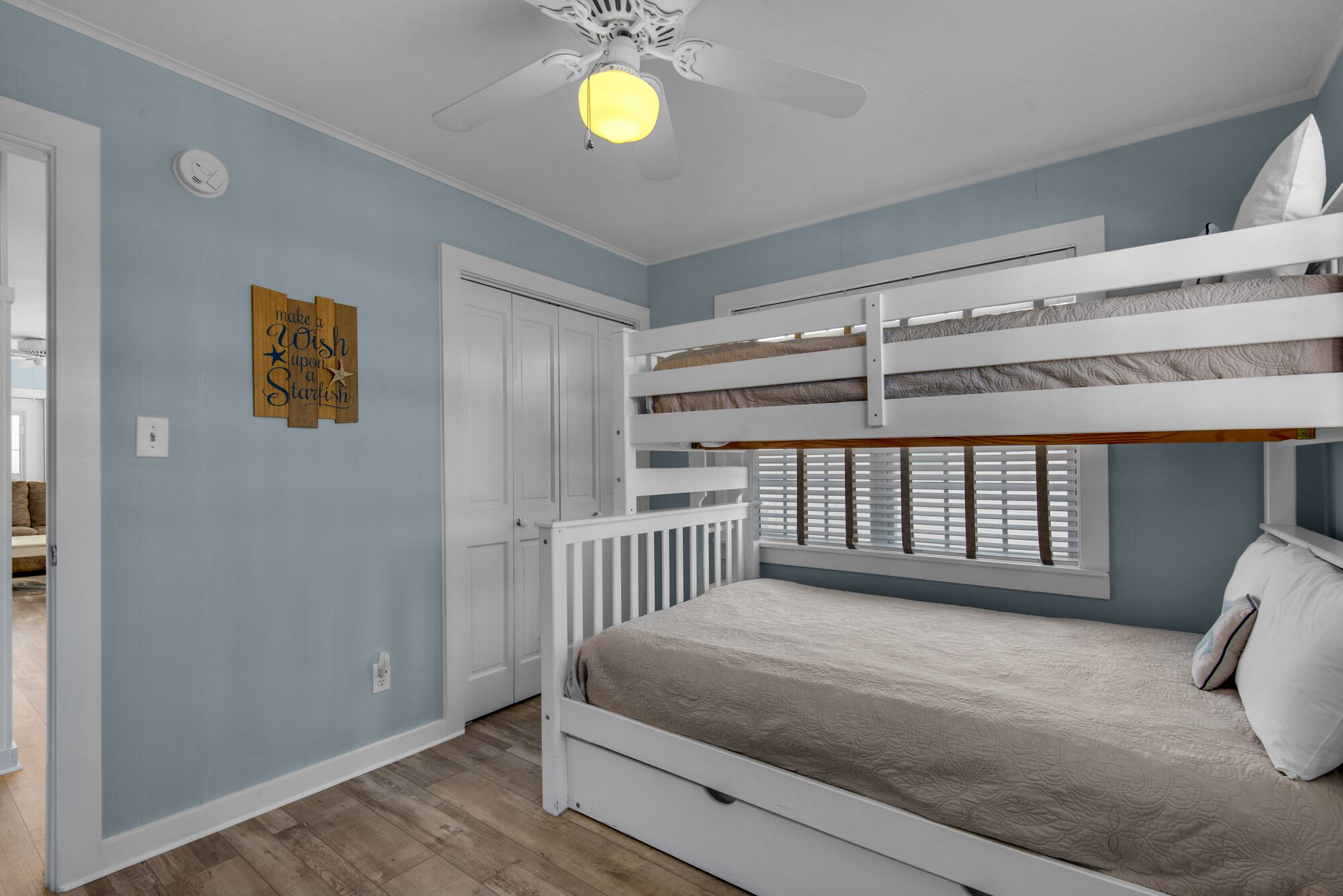 Une chambre avec un lit superposé, un ventilateur de plafond, une porte et une horloge murale.